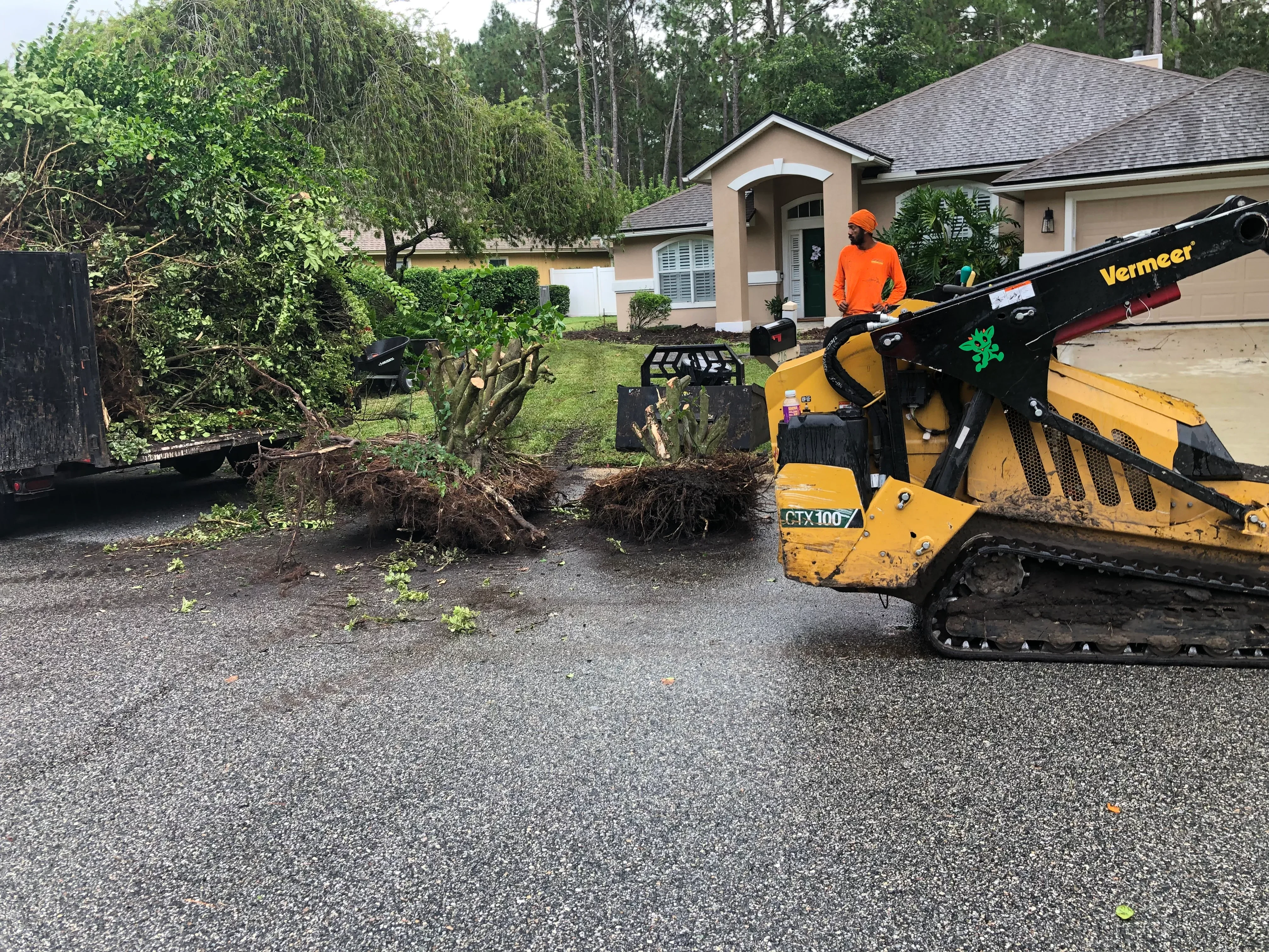 Vermeer skid steer with stump grinder removing tree and grinding stump in residential driveway