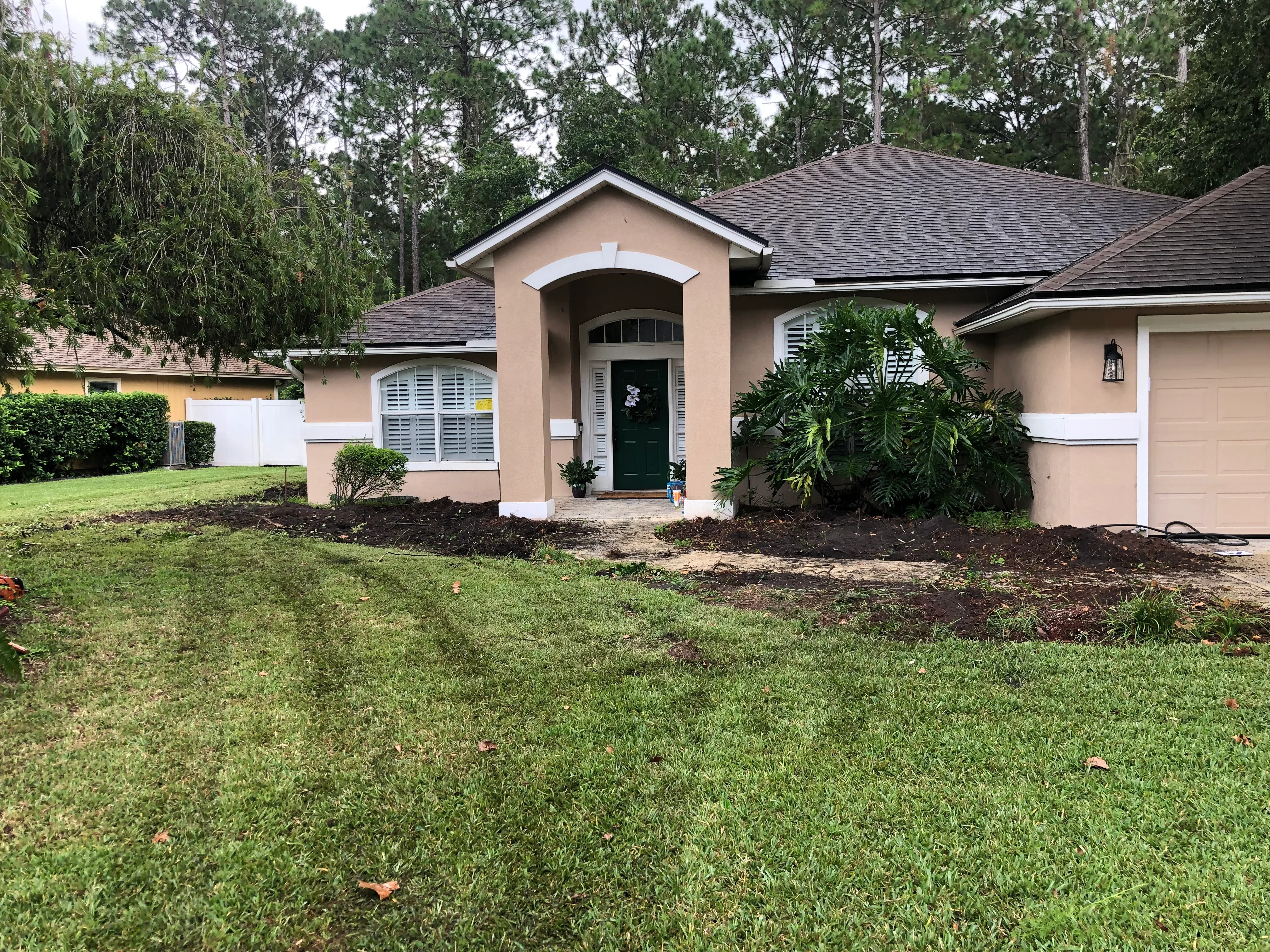 Front yard with fresh mulch beds, tropical plants, and manicured lawn around tan stucco home
