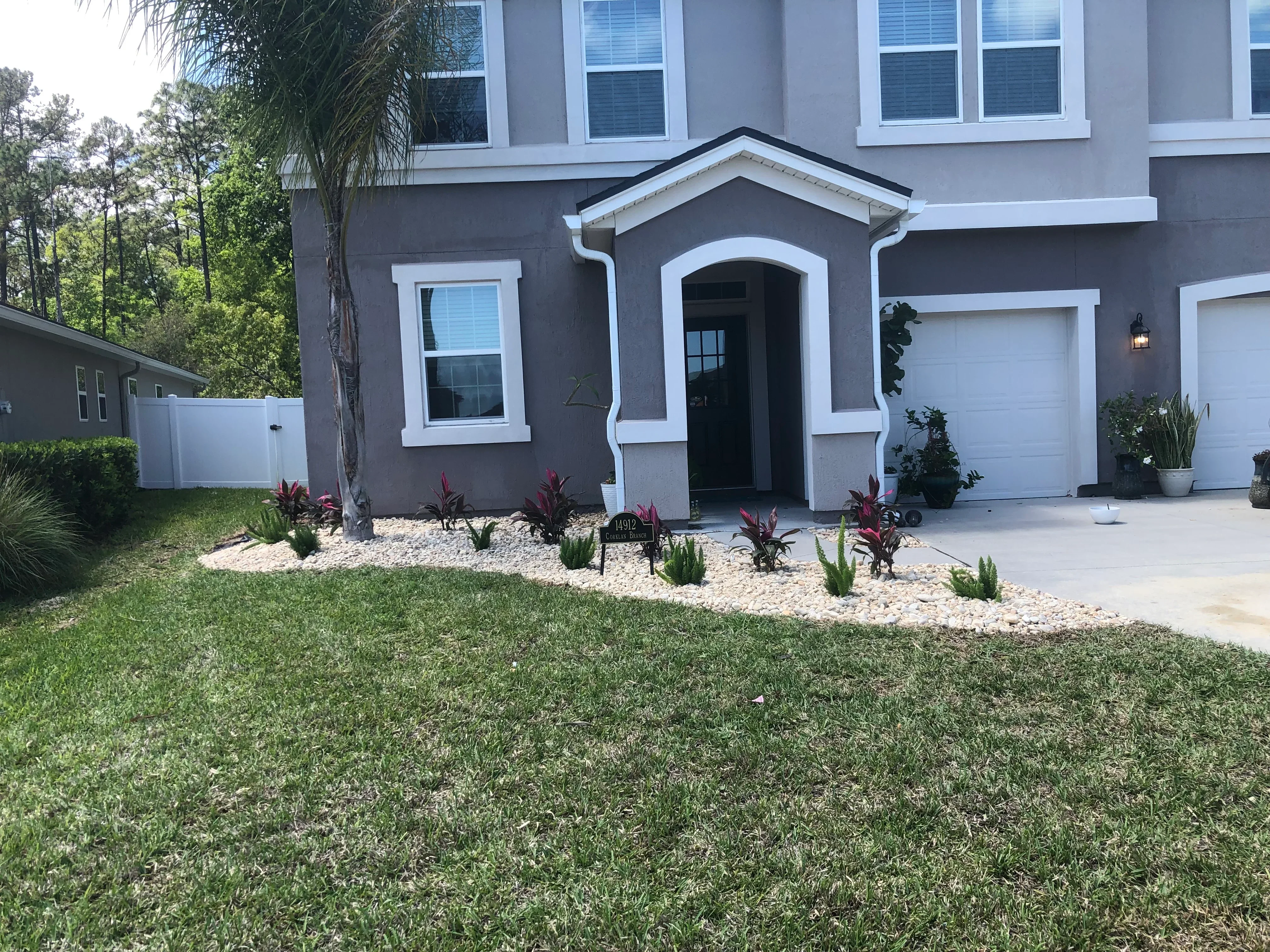 Fresh sod lawn with rock bed, tropical plants, and ornamental grasses along home entrance