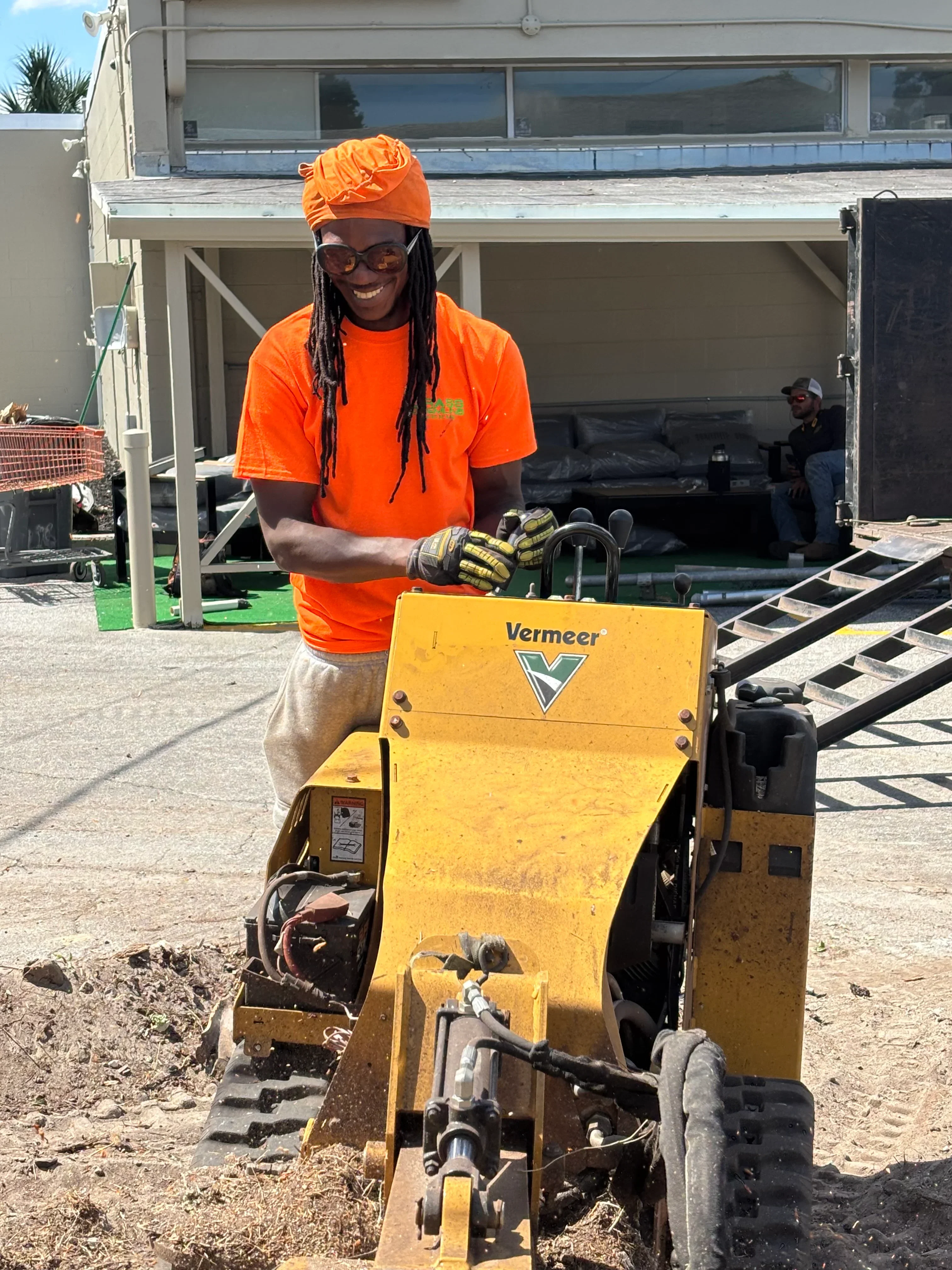 Operator in orange safety vest operating yellow Vermeer skid steer loader on job site