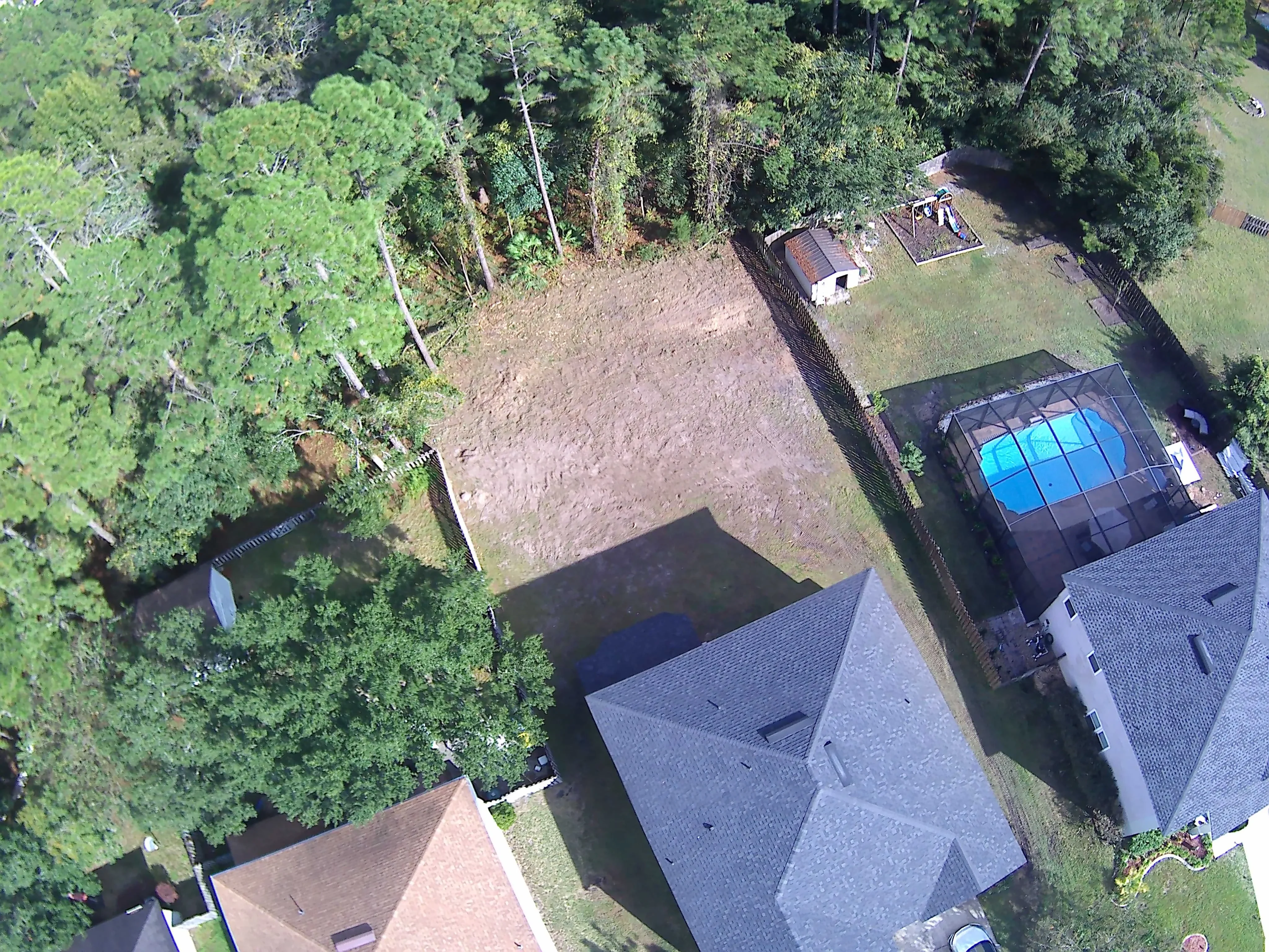 Aerial view of graded residential yard with prepared soil, mature trees, and pool enclosure