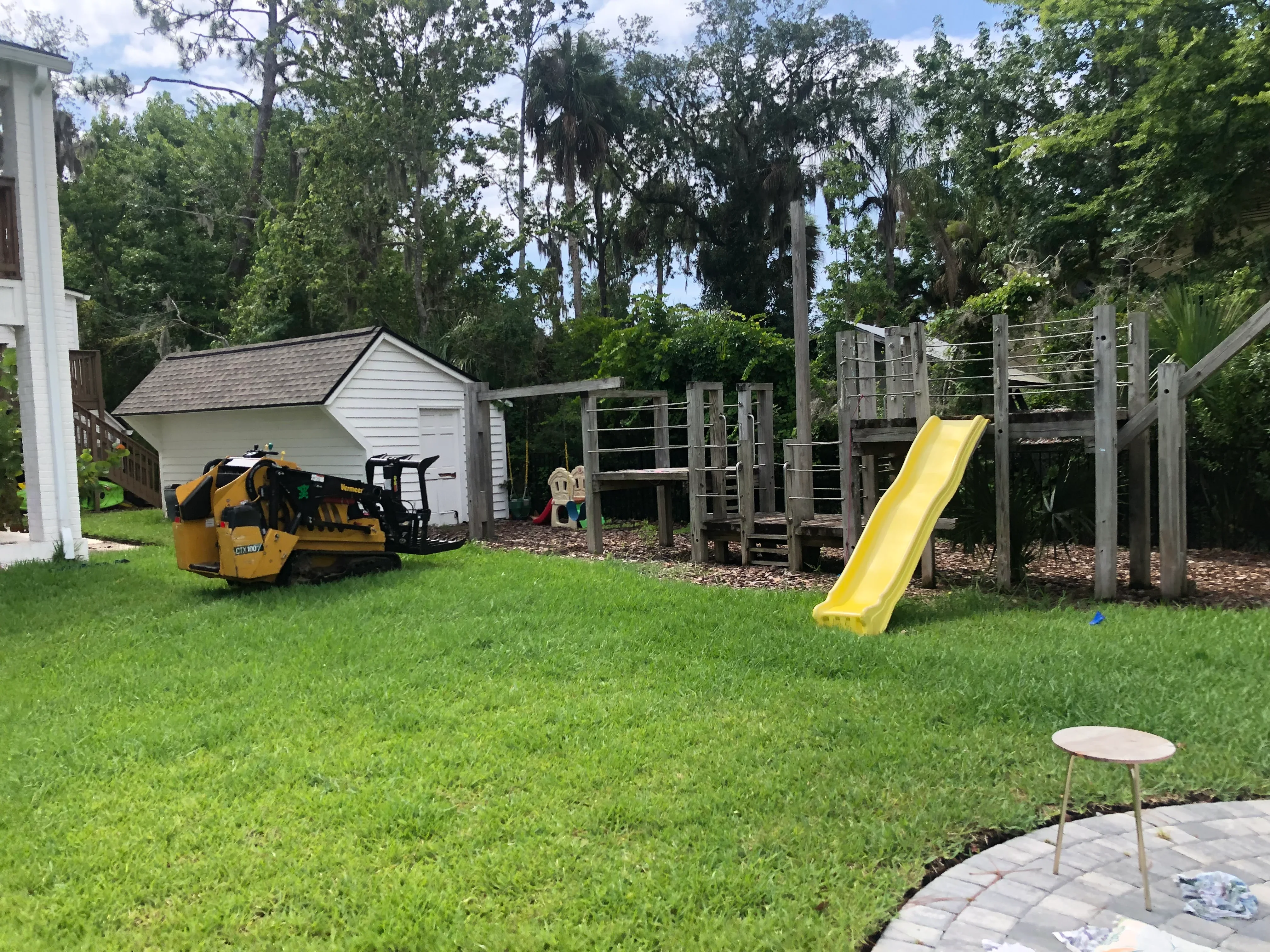 Freshly graded and sodded backyard with yellow playground slide and wooden play structure