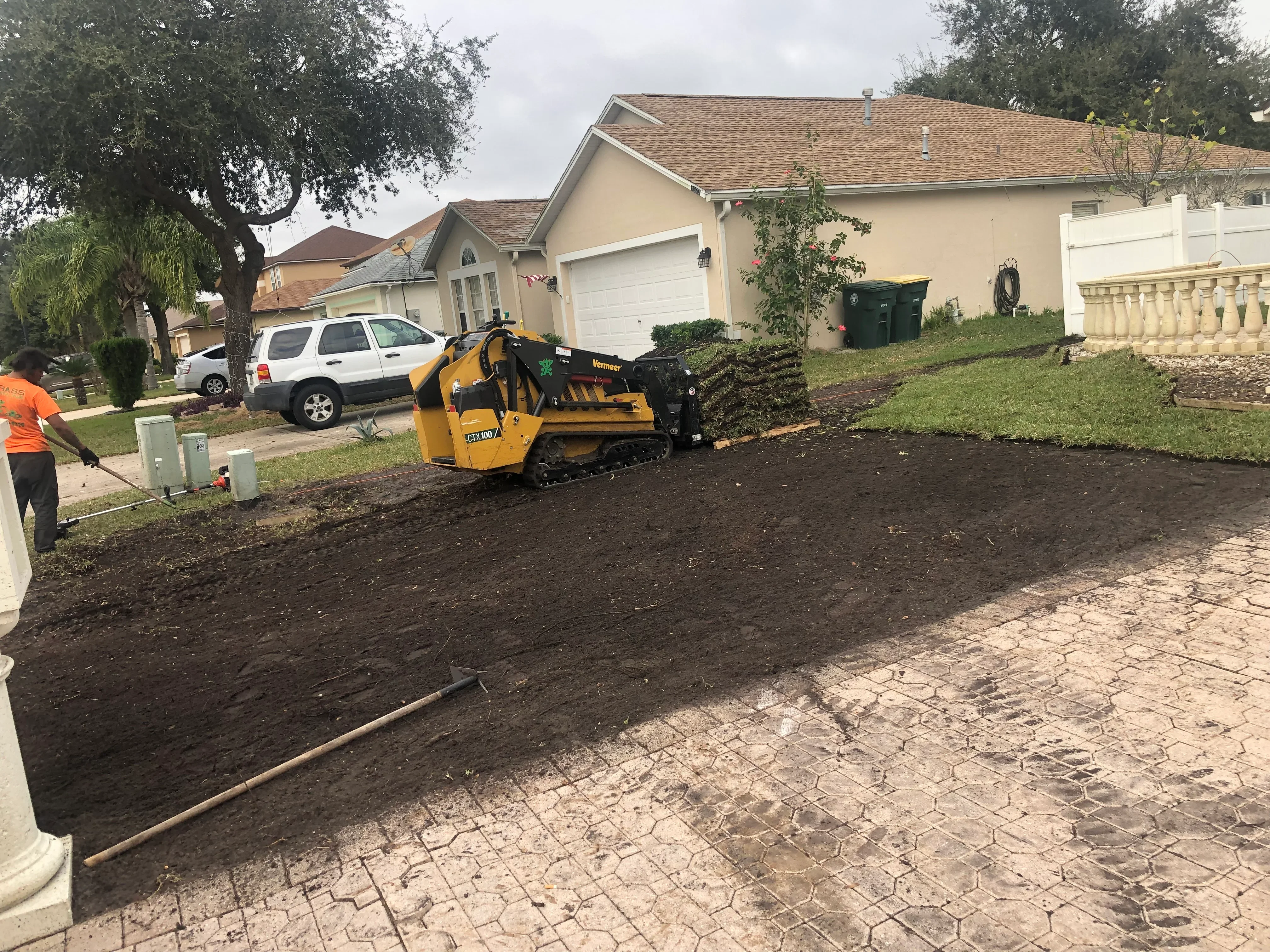 Compact track loader grading dark soil in residential front yard with paver edging