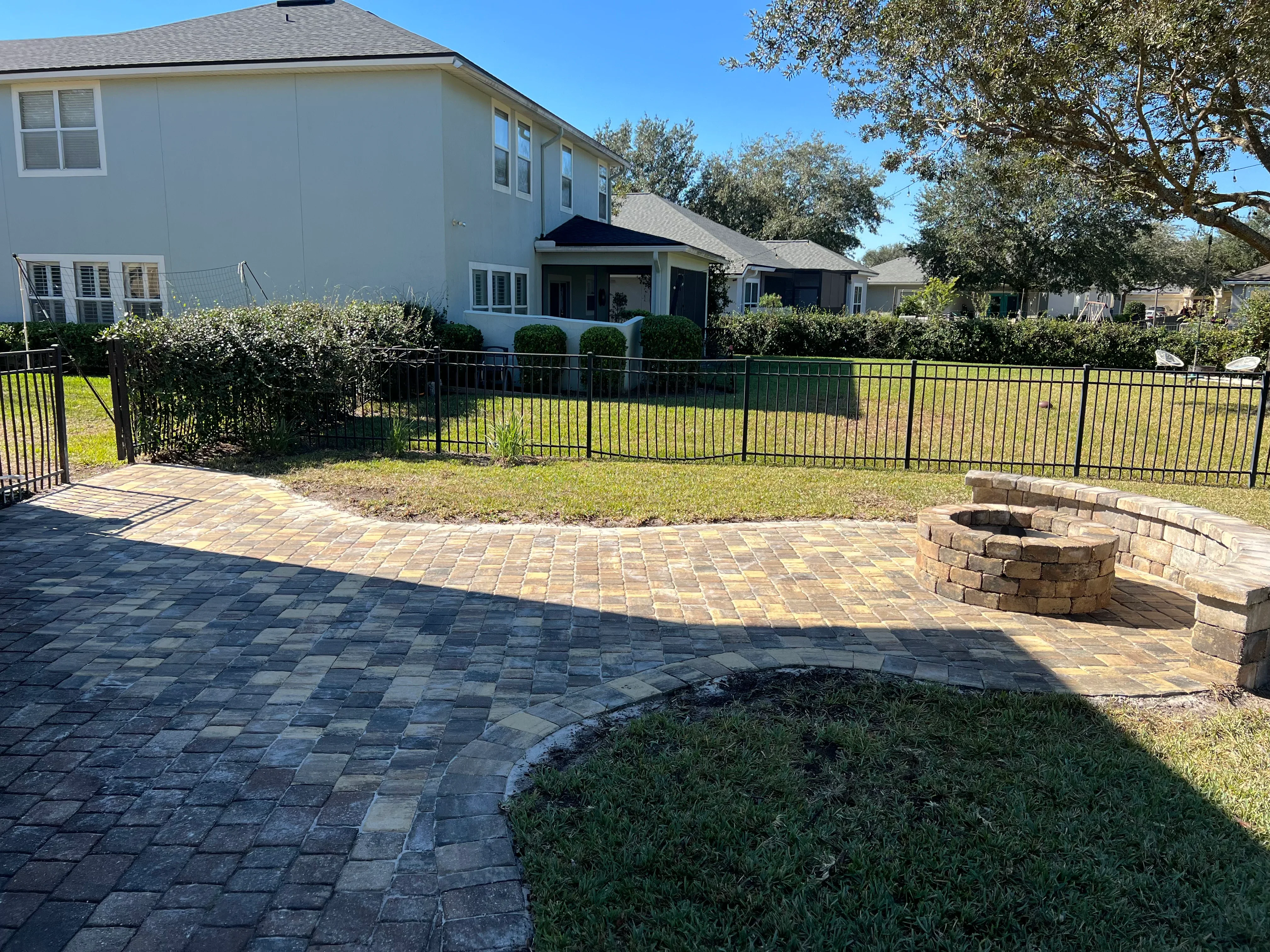 Paver patio with curved brick pattern, aluminum fencing, and brick seating wall