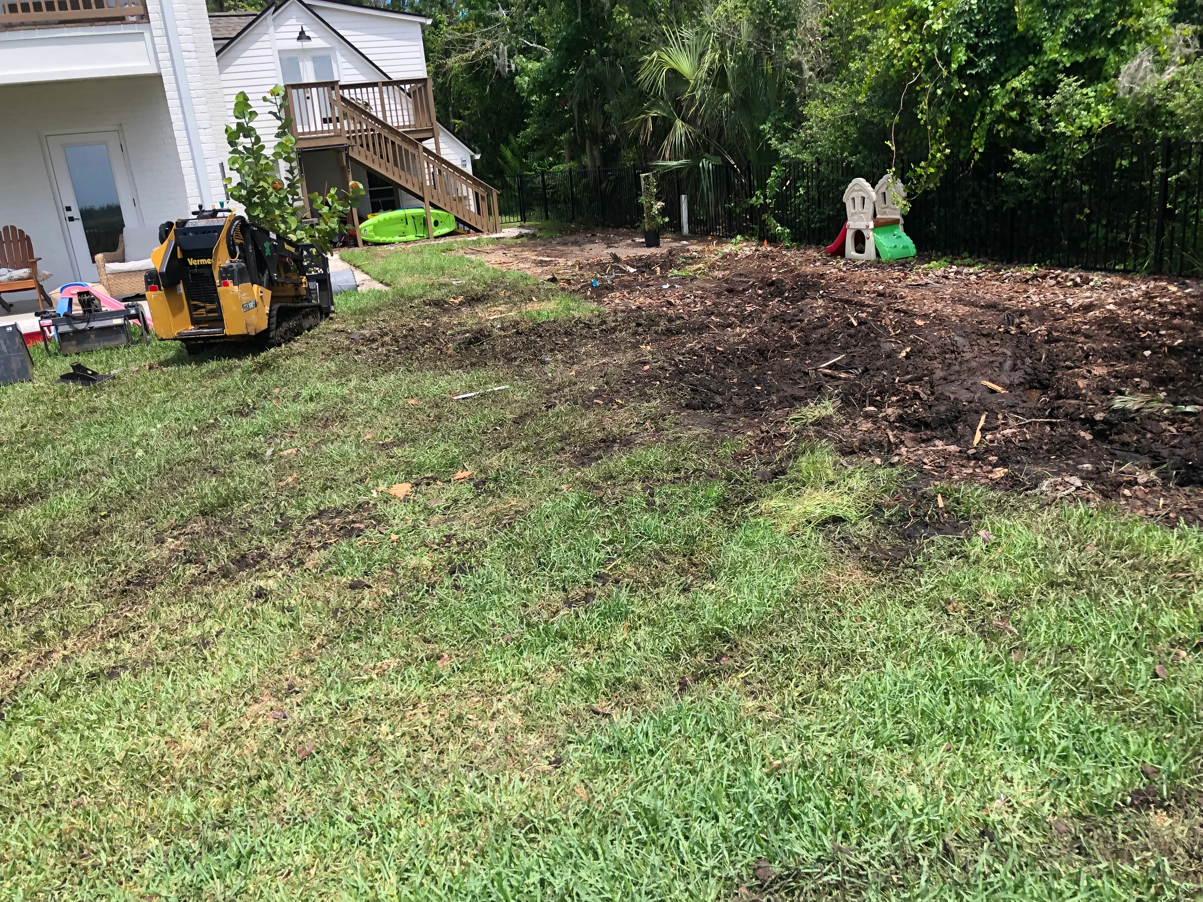 Backyard clearing with skid steer loader, mulch debris pile, and freshly graded lawn area